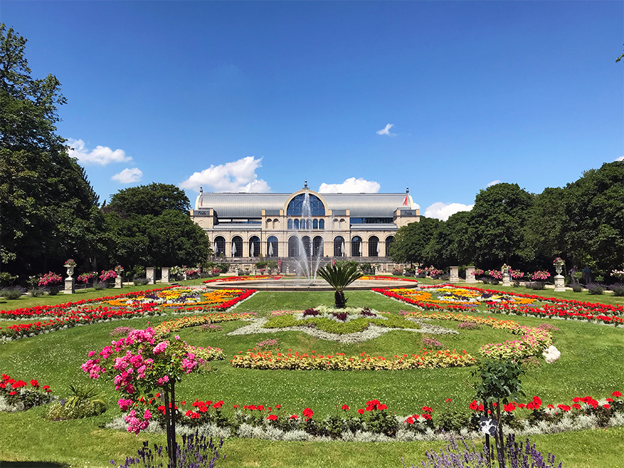 Die Flora, der Botanische Garten von Köln, mit bunten Blumenrabatten und knallblauem Sommerhimmel.