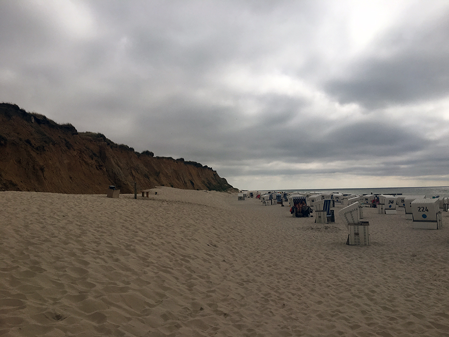 Links das Rote Kliff am Strand von Kampen, rechts die typischen weißen Strandkörbe und das Meer.