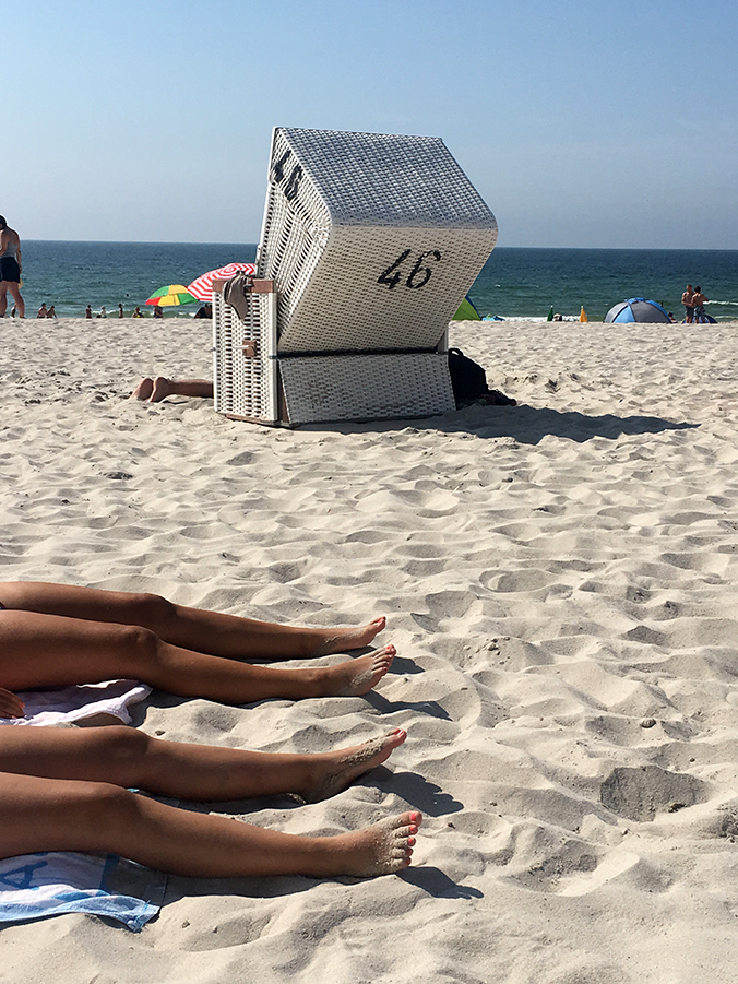 Die Farben Sylts: Nordseeblaues unendliches Meer, mattblauer Himmel, zartbeiger Sand, der nur hier ganz genau diese Farbe zu haben scheint, strahlendes Weiß für die Standkörbe und noch ein kleiner Klecks Schwarz für die Nummern hintendrauf. Und dazu braungebrannte Beine!