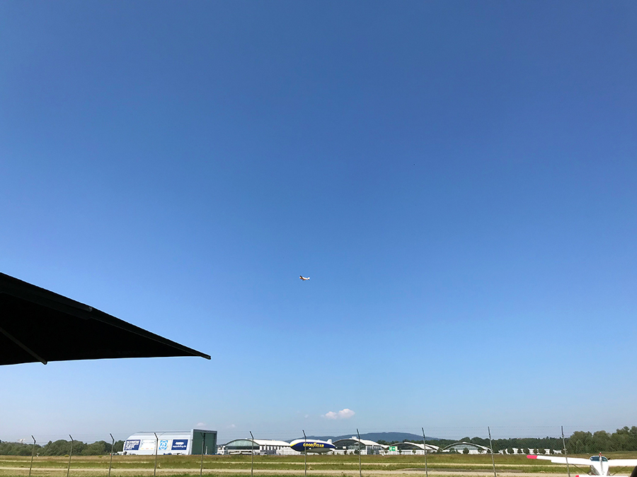 Oben in der Luft setzt gerade ein Flugzeug zum Landen an, und unten am Boden macht sich ein Zeppelin startklar.